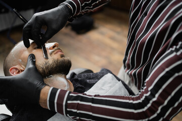 processes the beard shaving foam on the face, the client is a young man with dark hair. razor a...