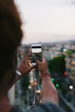 Back view of a young african american man taking a photo of Barcelona cityscape on his smartphone.