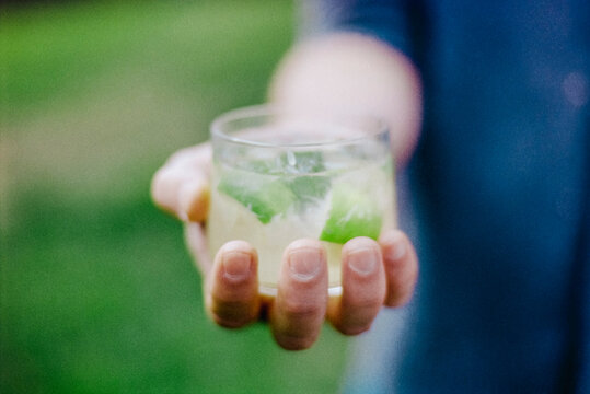 Hand holding Caipirinha cocktail outdoors