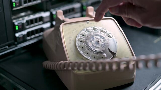 A man dials a number by clicking on the numbers of an old rotary dial telephone on the background of a server cabinet. Comic demonstration of outdated technologies