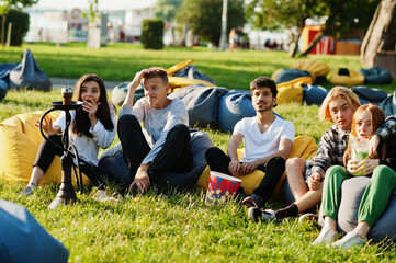 Young multi ethnic group of people watching movie at poof in open air cinema.
