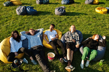 Young multi ethnic group of people watching movie at poof in open air cinema.