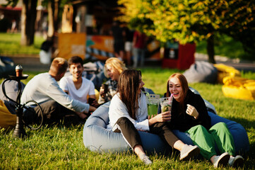 Young multi ethnic group of people watching movie at poof in open air cinema. Two girls with mojito...