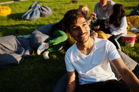 Young multi ethnic group of people watching movie at poof in open air cinema. Close up portrait of funny guy.