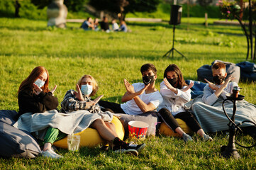 Young multi ethnic group of people watching movie at poof in open air cinema wear at mask during...
