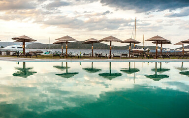Wooden sun umbrellas on the dge of the pool with reflection in the water