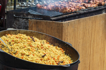 Healthy street food to go - in a large cauldron hot pilaf with pieces of meat and whole hot red pepper. Delicious food cooked over an open fire, which is offered at a street food fair, event, festival