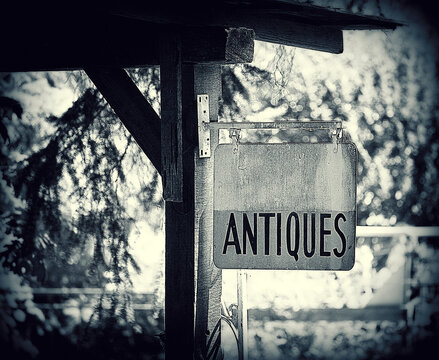 Black and white photo of an old Antiques Sign hanging on building