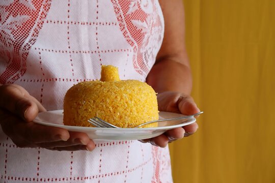 Woman's hands holding plate with Brazilian couscous (Cuscuz Brasileiro) on yellow background. Typical Brazilian breakfast. 