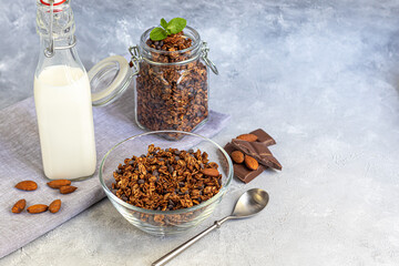 Homemade granola with strawberry pieces, chocolate and nuts in a glass jar. With the addition of milk or yogurt. On a gray background. Vegetarian dish.