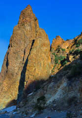 Cape Fiolent, high sharp ancient basalt rock stands on Black Sea coast, in the light of sunset with shadows against the backdrop of blue sky, Crimea