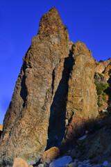 Cape Fiolent, high sharp ancient basalt rock, cliff stands on Black Sea stones coast, in the light of sunset with shadows against the backdrop of blue summer sky, Crimea