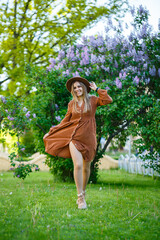 Obraz premium A girl in a brown hat and dress walks through the park, she has a European appearance and a smile on her face. Young attractive woman walks on a sunny day
