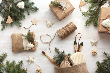 Zero waste Christmas flat lay with gifts in kraft paper and eco friendly products. Reusable sustainable recycled bath accessories in homemade burlap bag. Eco friendly new year decor with pine branches