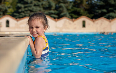 Naklejka premium Little girl in the pool. The girl is holding onto the side of the pool. Rest at the hotel