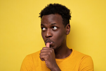 Fototapeta na wymiar African man with finger in mouth sucking thumb or biting fingernail in anxiety and stress, isolated on yellow background