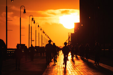 Large sun setting looking straight down a long boardwalk, with silhouettes of walkers and cyclists....
