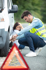 photo of man holding spare wheel against broken car