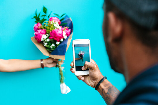 A man taking a photos of a bunch of flowers someone is holding up