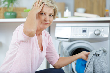 forgetful mature woman by washing machine holding jumper