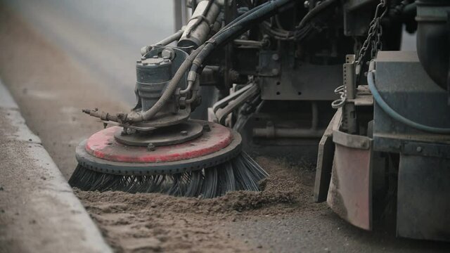 Industrial machine levels concrete dust with a sweeper on the side of the road