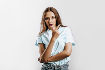 Young beautiful girl pointing finger to the side at on a white isolated background. A woman points to an idea, a place for advertising. Serious girl with fashion make-up with purple lips.