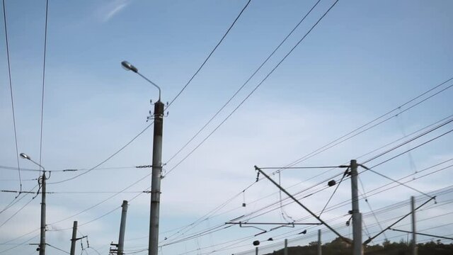 Bottom view of the electrical wires on the pole. Footage. Power supply networks of an industrial area against a blue sky. Passage cameras below them.