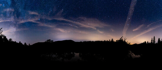 A panoramic view of Tarn Hows with the milky way & the plough in the cloudy night sky - obrazy, fototapety, plakaty
