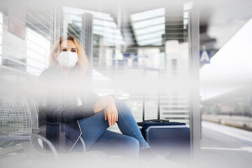 Eine Frau mit Maske wartet am Bahnhof, Maskenpflicht in der Öffentlichkeit 