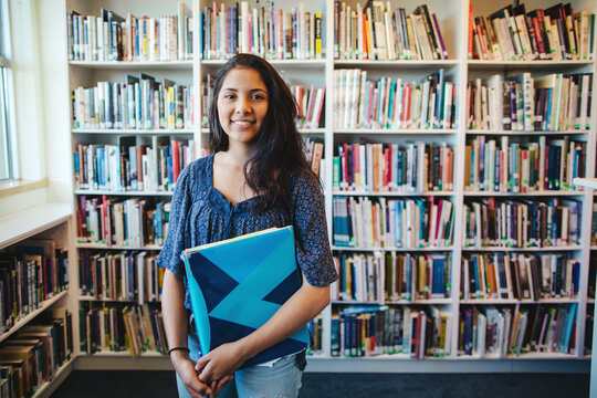 Portrait of happy high school teenage girl holding book binder in library