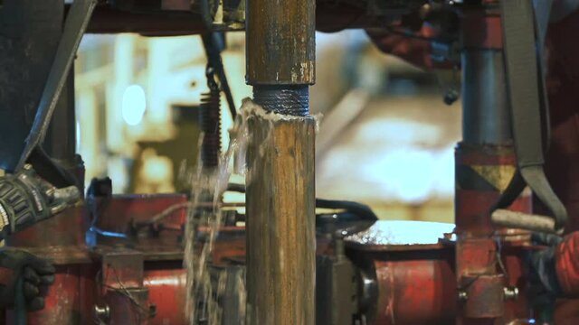 Connecting of drill pipes on the drilling platform. Water flows up from the well. In the background, two people bring equipment