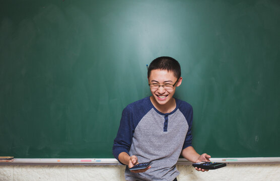 High school student standing in front of green chalkboard holding calculators and laughing