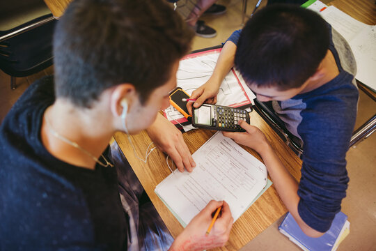 Real high school teenage boys working with calculator and learning together in classroom