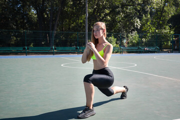 Young attractive girl in sportswear doing lunge exercise on the sports ground