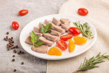 Boiled pork tongue with tomatoes and herbs on a gray concrete background. Side view, selective focus.