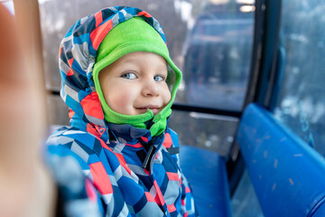 Cute adorable happy caucasian smiling small toddler kid boy enjoy ascent sitting inside ski lift gondola cable car and making selfie camera shot by smartphone. Winter travel with children concept