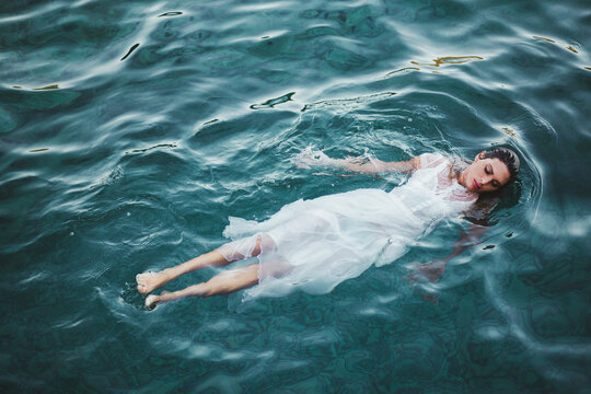 Young woman in a white dress floating on water