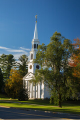 Obraz premium A traditional American White Church with high Steeple. Trees are showing autumn fall colors. Williamstown, MA