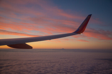 Wing of a commercial airliner at sunset shortly after take off.  Cloud layers are reflecting the pink in the sky.