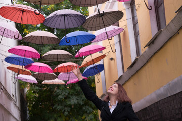Smiling beautiful woman walking at a street with multi colored umbrellas. Romantic girl pretending touch umbrella and fly on arrow streets.Traveler woman in Italy enjoing trip Dream and love concept