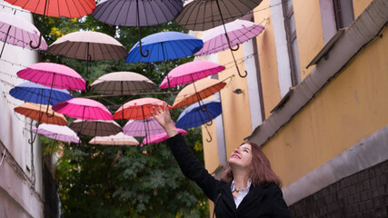 Smiling beautiful woman walking at a street with multi colored umbrellas. Romantic girl pretending touch umbrella and fly on arrow streets.Traveler woman in Italy enjoing trip Dream and love concept