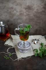 Tea with mint in a tall transparent glass on a ceramic stand. Hot warming aromatic drinks.