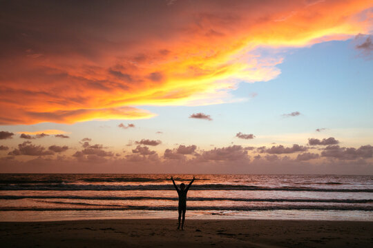Silhouette of a young boy with arms raised in V formation with a majestic twilight, sunset sky