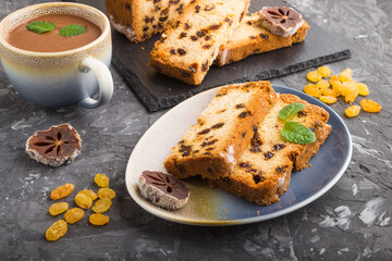 Homemade cake with raisins, dried persimmon and a cup of hot chocolate on a black concrete background. Side view, copy space.