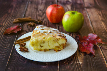 A piece of apple pie on a white plate. The table is decorated with apples, cinnamon and anise stars.