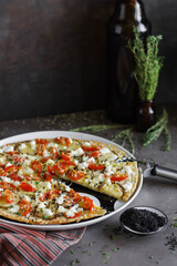 Big pizza with vegetables in a ceramic plate on a dark table.