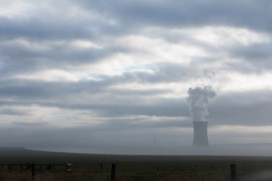 Chimney of power station on field under a cloudy sky