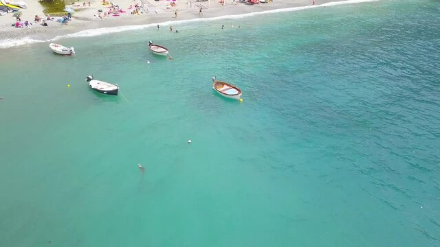 Panorama view of Monterosso al Mare village one of Cinque Terre in La Spezia, Italy. Drone moves away from the coast and people can be seen bawling at the bereu and the sea with boats.
