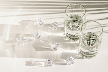 Transparent glasses and pieces of ice on white background. Bright sunlights and long hard shadows.