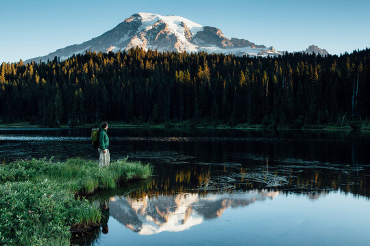 Man hiking along edge of Reflection Lakes with Mt. Rainier in distance, dawn